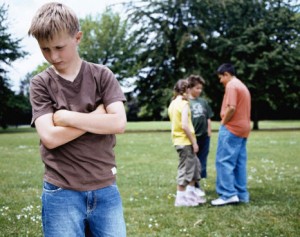 Boy (9-11) standing in park, arms crossed, group (10-12) in background