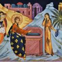 Un uomo è seduto vicino a un pozzo rosa. Ha un vestito con una manica rossa. La parte in basso del vestito è nera con delle stelle. Vicino al pozzo c'è una donna con un vestito giallo e una brocca blu in mano. Sullo sfondo ci sono montagne azzurre e gialle e una città