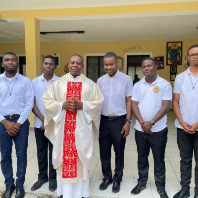 Sei uomini sono allineati per una foto. Alle loro spalle si vede un edificio giallo.