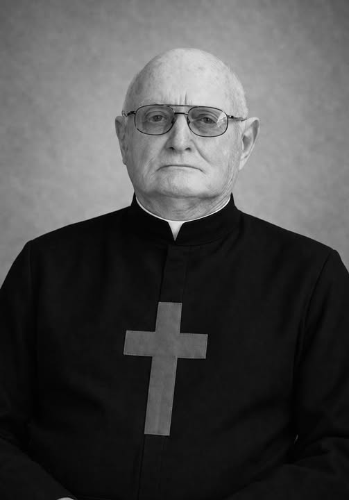 immagine in bianco e nero del padre Eric James Perret. Hu vestito da sacerdote nero con una croce sul petto.