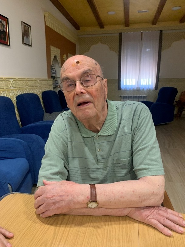 Foto a colori di P. Joaquin Morant Garcia. E' seduto davanti a un tavolo di legno, indossa una maglietta verde senza maniche. Sullo sfondo ci sono delle sedie blu e una finestra con delle tende bianche.