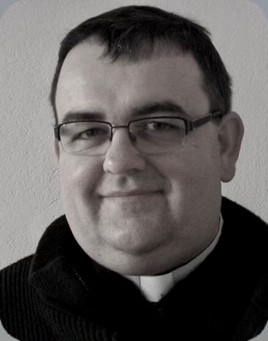 Primo piano in bianco e nero di padre Tomasz Stanchon, sacerdote polacco camilliano. L'uomo ha l'abito da sacerdote e gli occhiali