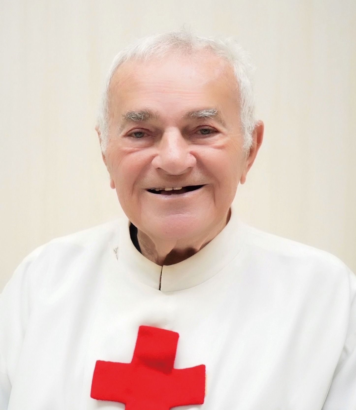 Immagine di padre Michielini anziano, è vestito di bianco, ha una croce rossa sul petto. Lo sfondo è bianco.