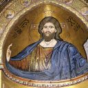 Nell'immagine c'è un uomo con la barba e un vestito blu. La mano destra benedice con tre dita in alto e due chiuse. Nell'altra mano ha un libro scritto in greco. Lo sfondo è dorato