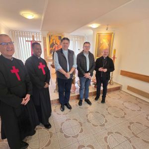 cinque uomini tra cui padre Tramontin, superiore generale dei camilliani, posano per una foto davanti a immagini della Madonna e di Cristo. Due uomini indossano la tunica nera dei camilliani con la croce rossa sul petto