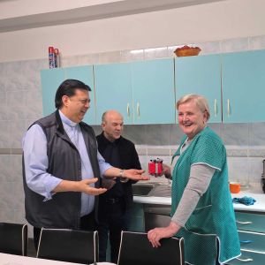 Padre Pedro Tramontin, superiore generale dei camilliani, insieme a un uomo vestito di nero e auna donna con un grembiule azzurro. Sullo sfondo c'è una cucina azzurra