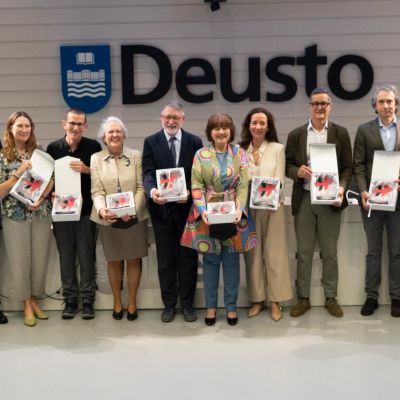 dodici persone, uomini e donne, mostrano la trga bianca di un premio che hanno ricevuto. Dietro di loro c'è il logo dell'università di Desto che si trova a Bilbao, in Spagna