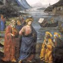 Un uomo vestito di blu con l'aureola è circodato dalla folla. Dietro di lui si vedono delle barche.