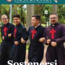Quattro uomini vestiti con una tunica nera da prete camminano a braccetto sorridendo. Hanno tutti una croce rossa camilliana sul petto. Sullo sfondo ci sono degli alberi. Il pavimento è in mattonato marrone chiaro.