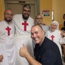 Due sacerdoti e una suora, tutti vestiti di bianco con la croce rossa di san Camillo, sono in posa per una foto. Sullo sfondo ci sono delle pareti gialle