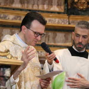 Un uomo vestito di bianco celebra la messa. Accanto a lui un uomo vestito di bianco tiene il microfono