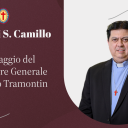 Un uomo con capelli neri, giacca nera e camicia azzurra è in posa per una una foto frontale. Ha al collo una catenina con la croce rossa di San Camillo