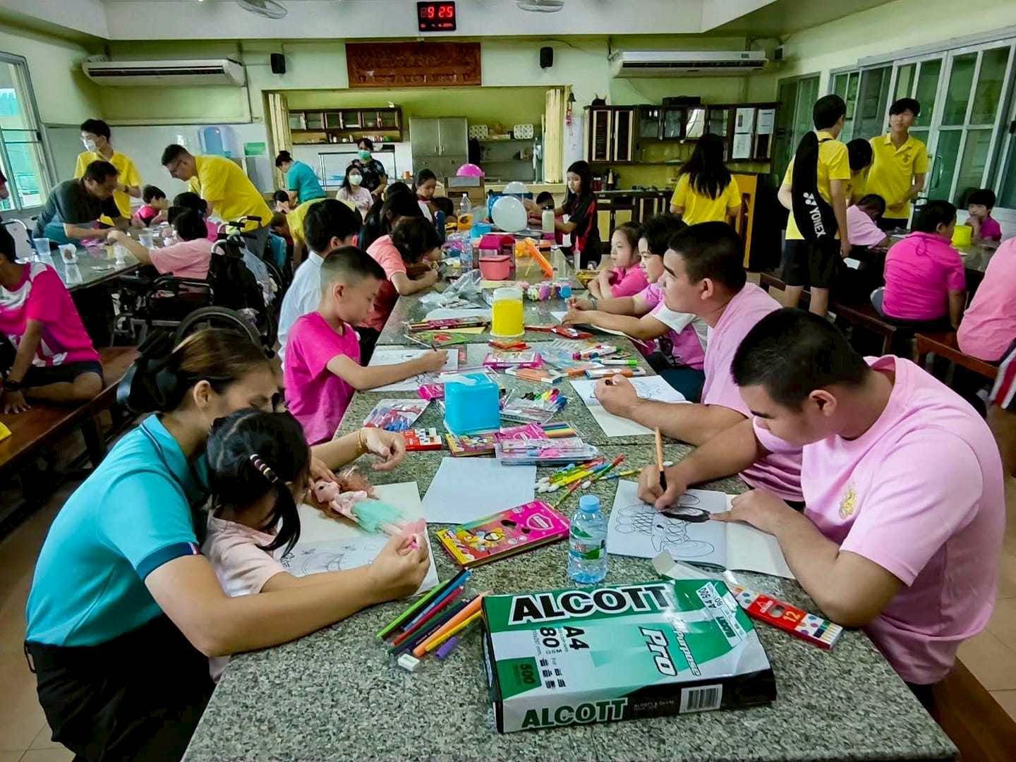 Nella foto ci sono ragazzi e ragazze che dipingono. Sono seduti a un tavolo all'interno di una stanza verde