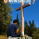 Un unomo con i capellis curi, la maglietta blu a mezze maniche e i pantaloni scuri, prega il rosario mentre è seduto su un sasso. Davanti a lui c'è una croce di legno chiaro. Sullo sfondo ci sono degli alberi. Il cielo è azzurro intenso. Il terreno e marrone. Sulla foto ci sono le scritte: Newsletter - Il mondo camilliano visto da Roma e Roma vista dal mondo camilliano. In basso c'è la scritta Ricerca di Dio nella bellezza del creato.