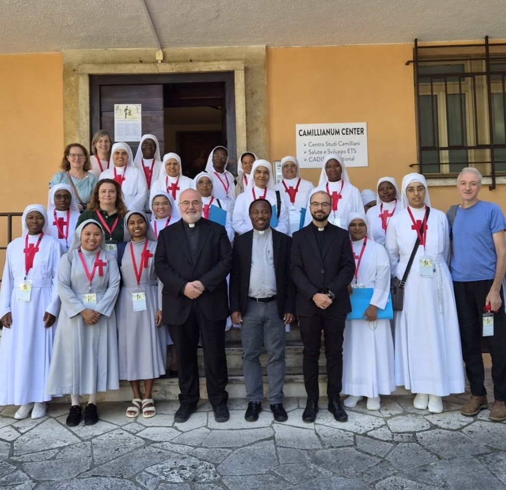 Un gruppo di persone, soprattutto suore vestite di bianco con la croce rossa di San Camillo, posano in piedi su una scalinata per una foto.