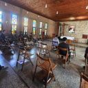 Alcuni uomini sono seduti in chiesa di saplle con un libro in mano. Il tetto della chiesa è di legno. Sullo sfondo c'è un'immagine di San Camillo De Lellis.