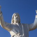 Una statua bianca di Cristo ha le mani alzate. La statua si trova all'aperto. Intorno si vede solo il cielo azzurro quasi viola