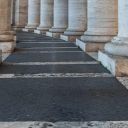 Colonnato con colonne. Nella foto si vede solo la base della colonna con il piedistallo. Al centro c'è una strada nera con delle strisce bianche