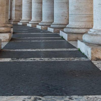 Colonnato con colonne. Nella foto si vede solo la base della colonna con il piedistallo. Al centro c'è una strada nera con delle strisce bianche